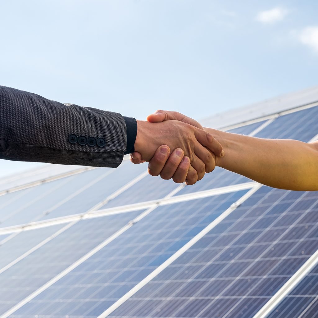 dos-personas-con-un-apreton-de-manos-contra-el-panel-solar-despues-de-la-celebracion-del-acuerdo-en-las-energias-renovables